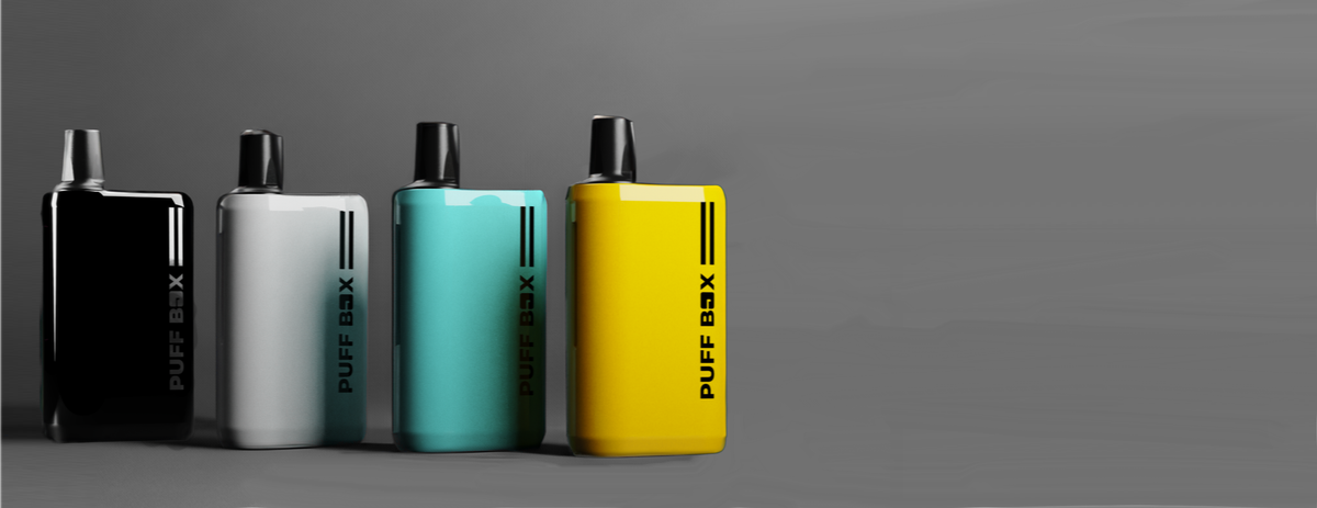 Four Puff Box devices in different colours (black, white, teal, yellow) standing upright in a line, on a light grey gradient background